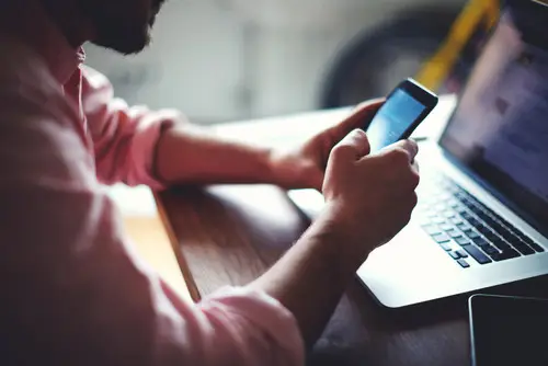 Pessoa usando smartphone e laptop para comunicação e negócios.
